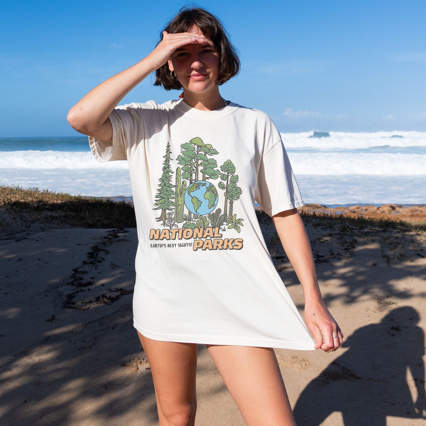 Person wearing a white t-shirt with 'National Parks' design on a beach