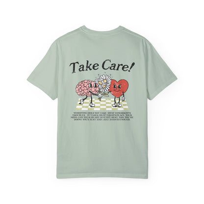 Graphic tee featuring a whimsical design with a heart and brain holding a flower, paired with motivational text encouraging self-care and positivity. Perfect for mental health awareness and retro-inspired casual style.