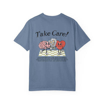 Graphic tee featuring a whimsical design with a heart and brain holding a flower, paired with motivational text encouraging self-care and positivity. Perfect for mental health awareness and retro-inspired casual style.