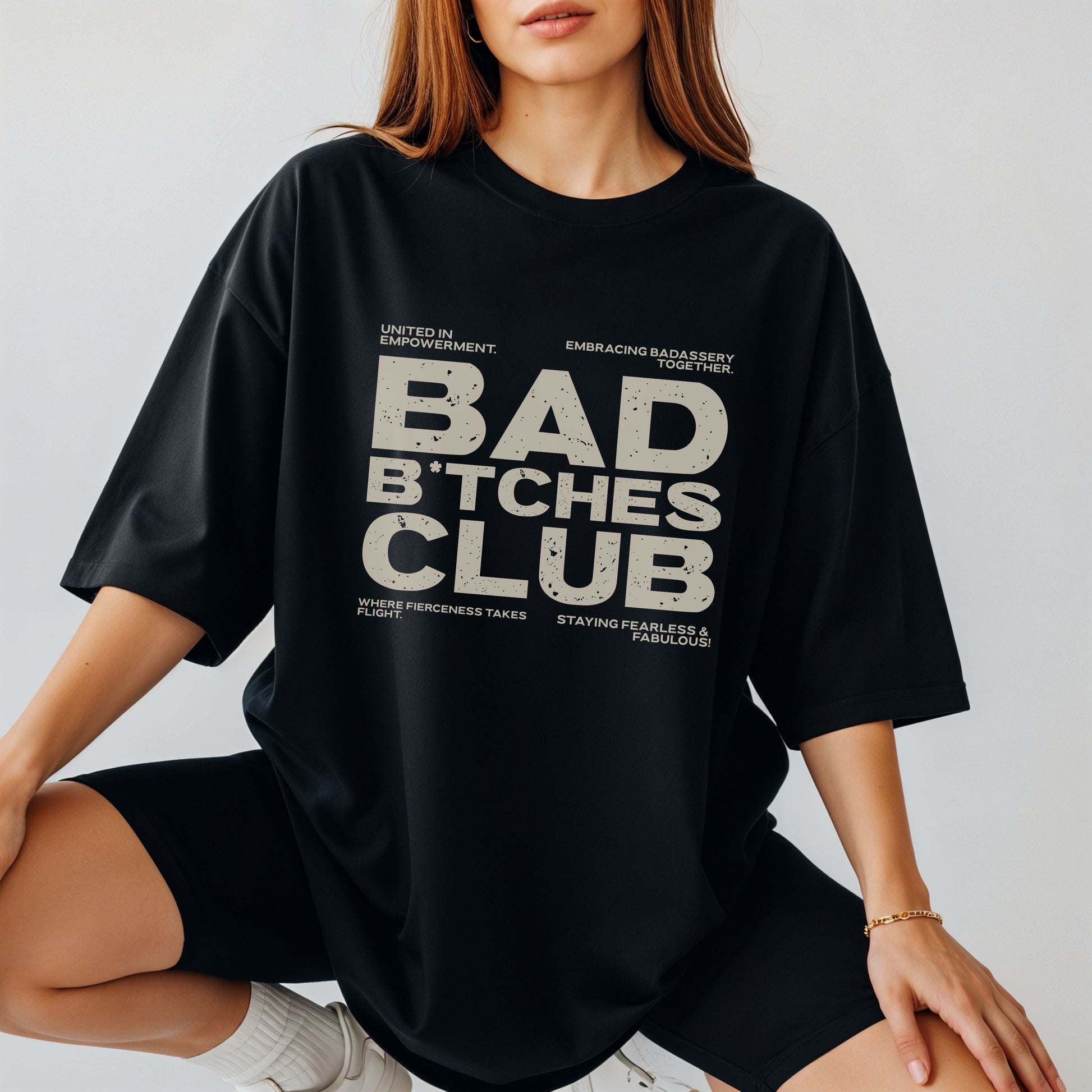 Person wearing a black t-shirt with 'BAD B*TCHES CLUB' text on a plain background