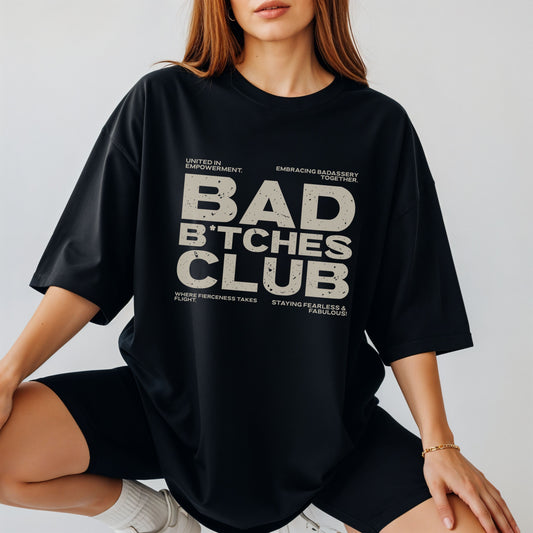Person wearing a black t-shirt with 'BAD B*TCHES CLUB' text on a plain background