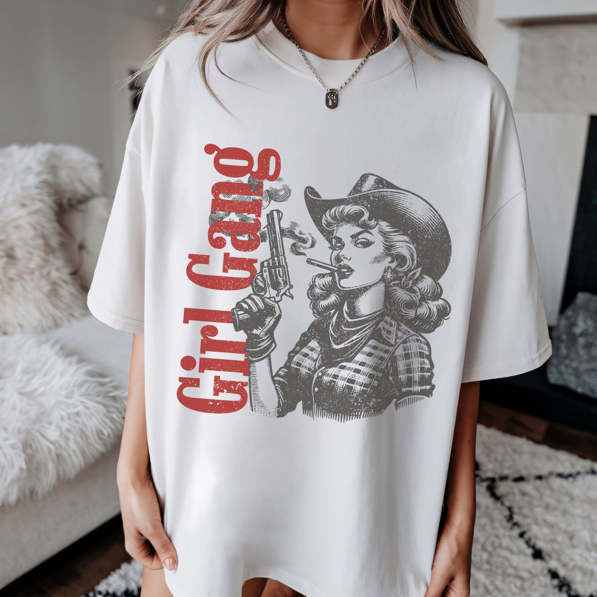 White t-shirt with graphic design of a woman in a cowboy hat and plaid shirt, holding a gun and smoking a cigarette, with 'Girl Gang' text.
