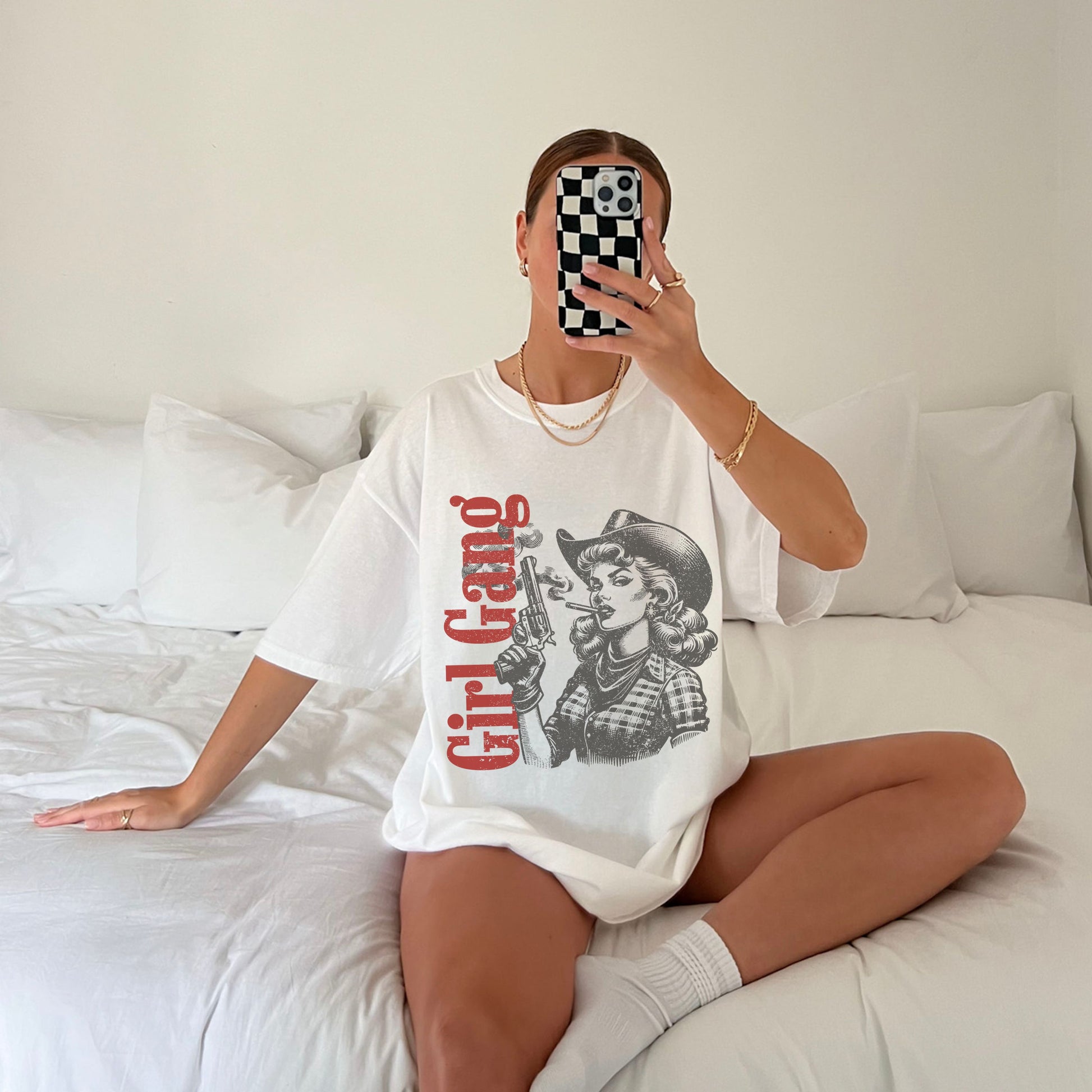 Person wearing a white t-shirt with 'Girl Gang' graphic sitting on a bed.