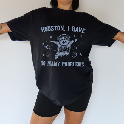 Person wearing a black t-shirt with a graphic and text 'Houston, I have so many problems' on a white background