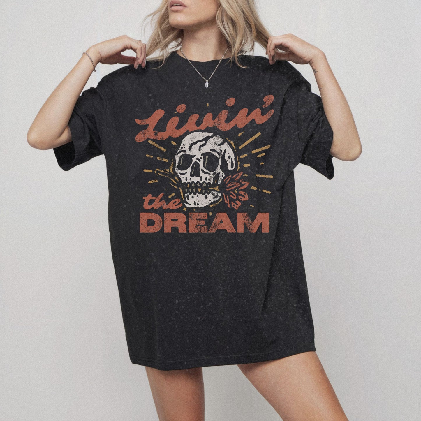 Black t-shirt with a vintage skull graphic, sunburst design, and 'Livin' the Dream' text in retro font. Perfect for a retro skull t-shirt or distressed skull tee look with a boho rocker vibe. Casual vintage t-shirt style for edgy everyday wear.