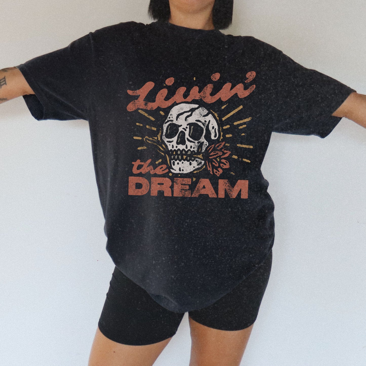 Black t-shirt with a vintage skull graphic, sunburst design, and 'Livin' the Dream' text in retro font. Perfect for a retro skull t-shirt or distressed skull tee look with a boho rocker vibe. Casual vintage t-shirt style for edgy everyday wear.
