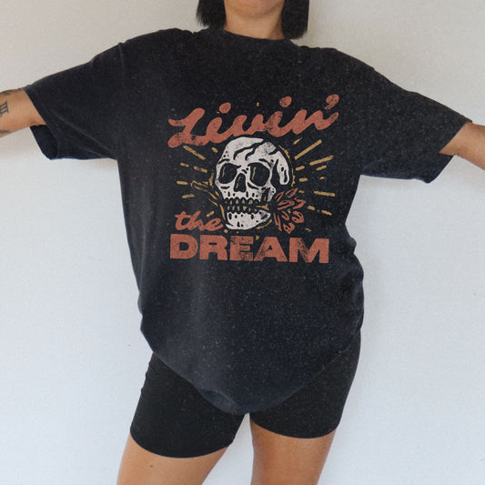 Black t-shirt with a vintage skull graphic, sunburst design, and 'Livin' the Dream' text in retro font. Perfect for a retro skull t-shirt or distressed skull tee look with a boho rocker vibe. Casual vintage t-shirt style for edgy everyday wear.