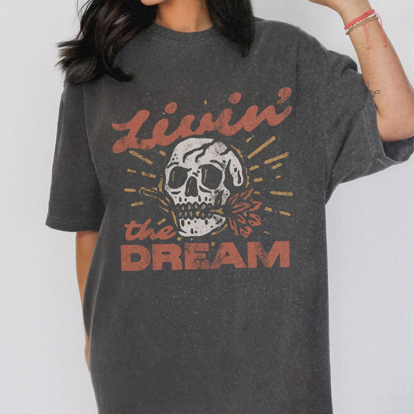 Black t-shirt with a vintage skull graphic, sunburst design, and 'Livin' the Dream' text in retro font. Perfect for a retro skull t-shirt or distressed skull tee look with a boho rocker vibe. Casual vintage t-shirt style for edgy everyday wear.
