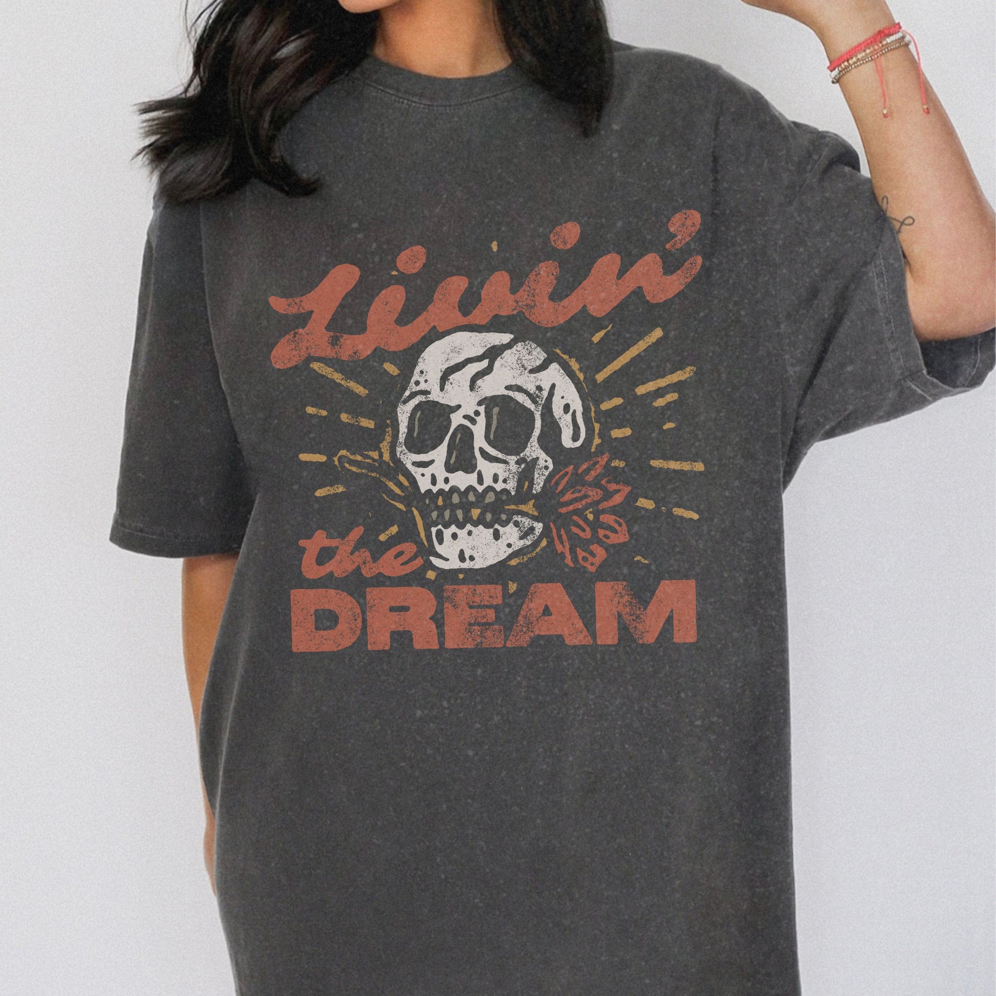 Black t-shirt with a vintage skull graphic, sunburst design, and 'Livin' the Dream' text in retro font. Perfect for a retro skull t-shirt or distressed skull tee look with a boho rocker vibe. Casual vintage t-shirt style for edgy everyday wear.
