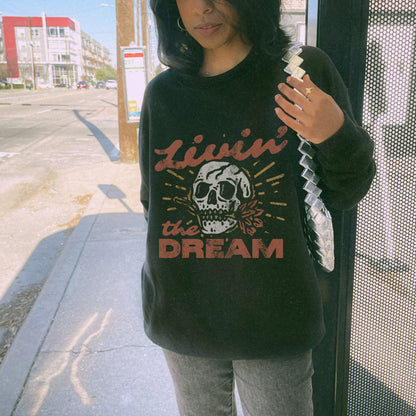 Oversized retro skull sweatshirt with bold vintage-inspired design. Livin' The Dream shirt featuring edgy graphic details. Perfect boho skull pullover for grunge and aesthetic styles. Casual vintage skull sweater ideal for layering and everyday wear. 