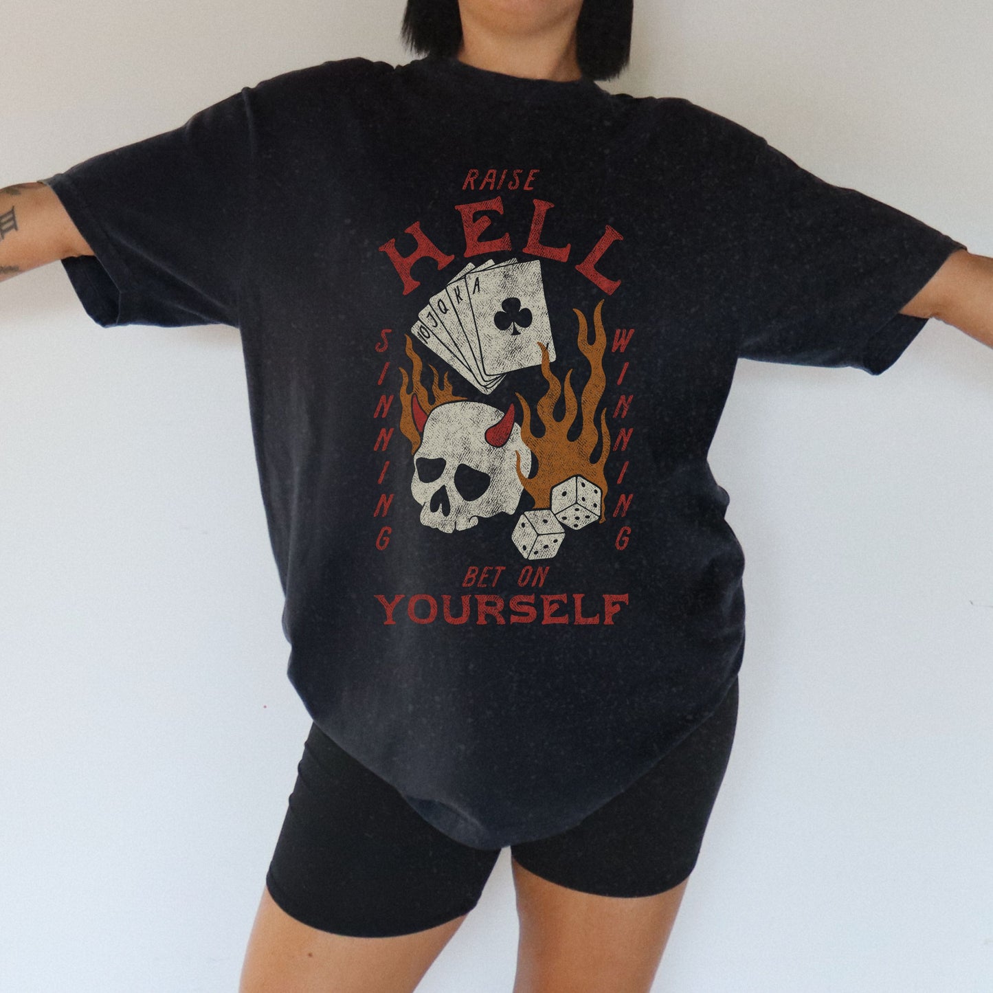 Vintage skull tee with a hellfire graphic, outlaw poker design, and flaming dice. Edgy gambling shirt with tattoo style skull, gothic aesthetic, and punk rock vibe. Retro casino shirt for risk-takers who love badass dice graphics and dark streetwear fashion.
