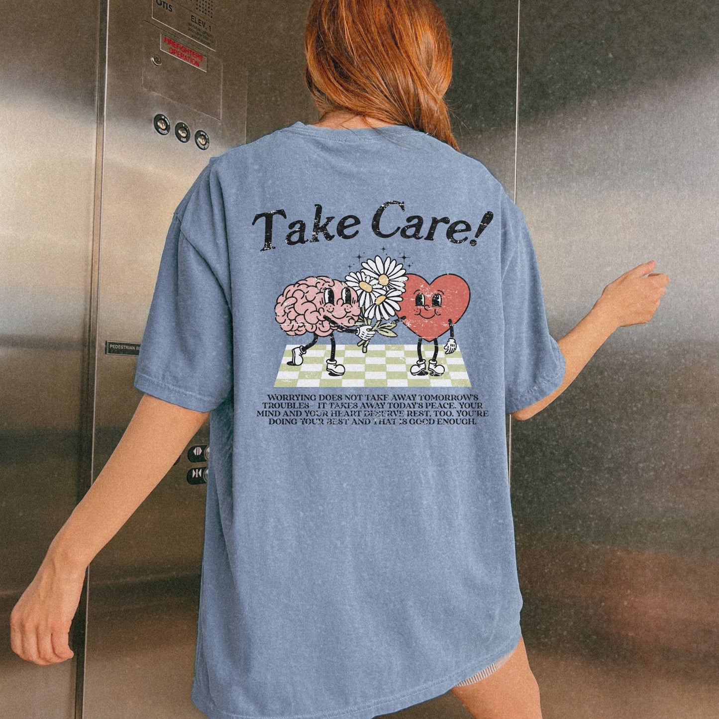 Graphic tee featuring a whimsical design with a heart and brain holding a flower, paired with motivational text encouraging self-care and positivity. Perfect for mental health awareness and retro-inspired casual style.