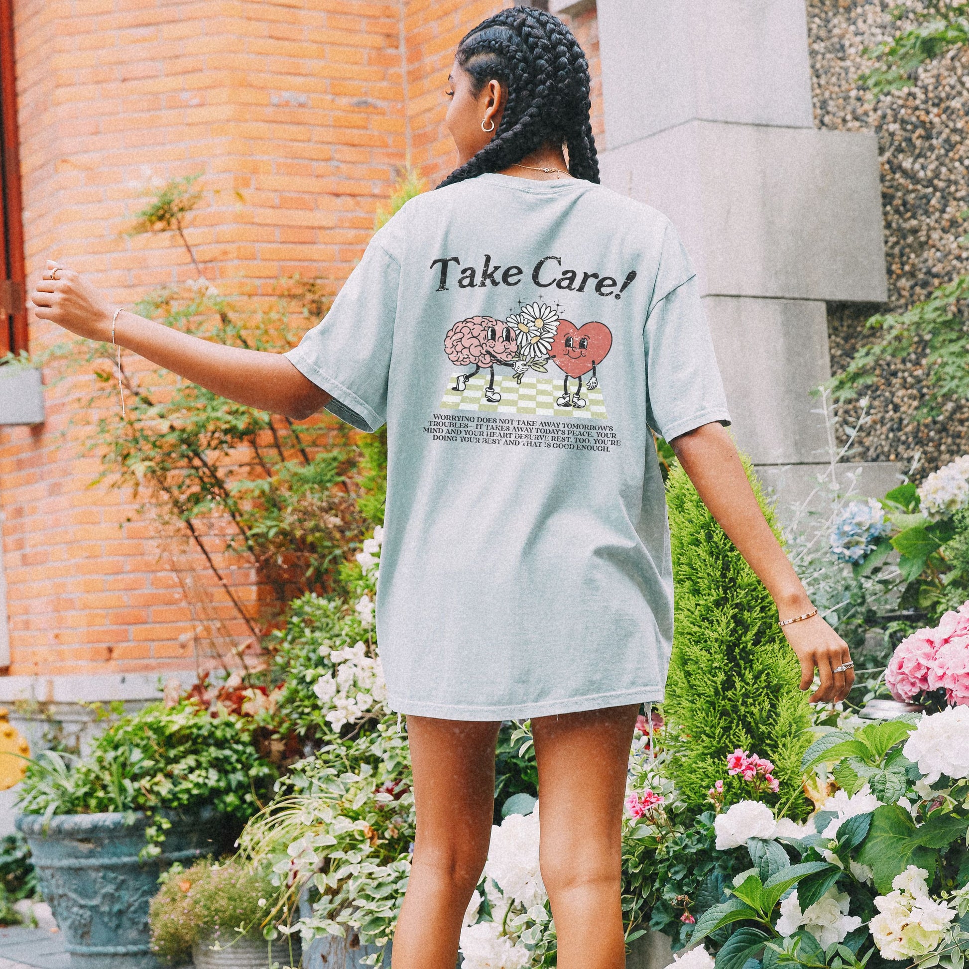 Graphic tee featuring a whimsical design with a heart and brain holding a flower, paired with motivational text encouraging self-care and positivity. Perfect for mental health awareness and retro-inspired casual style.