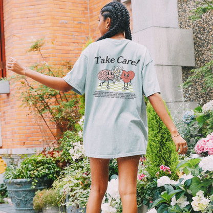 Graphic tee featuring a whimsical design with a heart and brain holding a flower, paired with motivational text encouraging self-care and positivity. Perfect for mental health awareness and retro-inspired casual style.