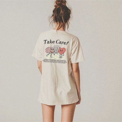 Graphic tee featuring a whimsical design with a heart and brain holding a flower, paired with motivational text encouraging self-care and positivity. Perfect for mental health awareness and retro-inspired casual style.
