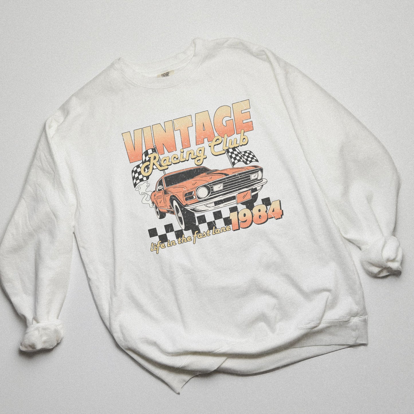 Retro car club shirt with vintage 1984 race car graphic, distressed design, and checkered flag accents. Perfect for muscle car lovers and fans of classic racing. Available as a crewneck sweatshirt in multiple colors.