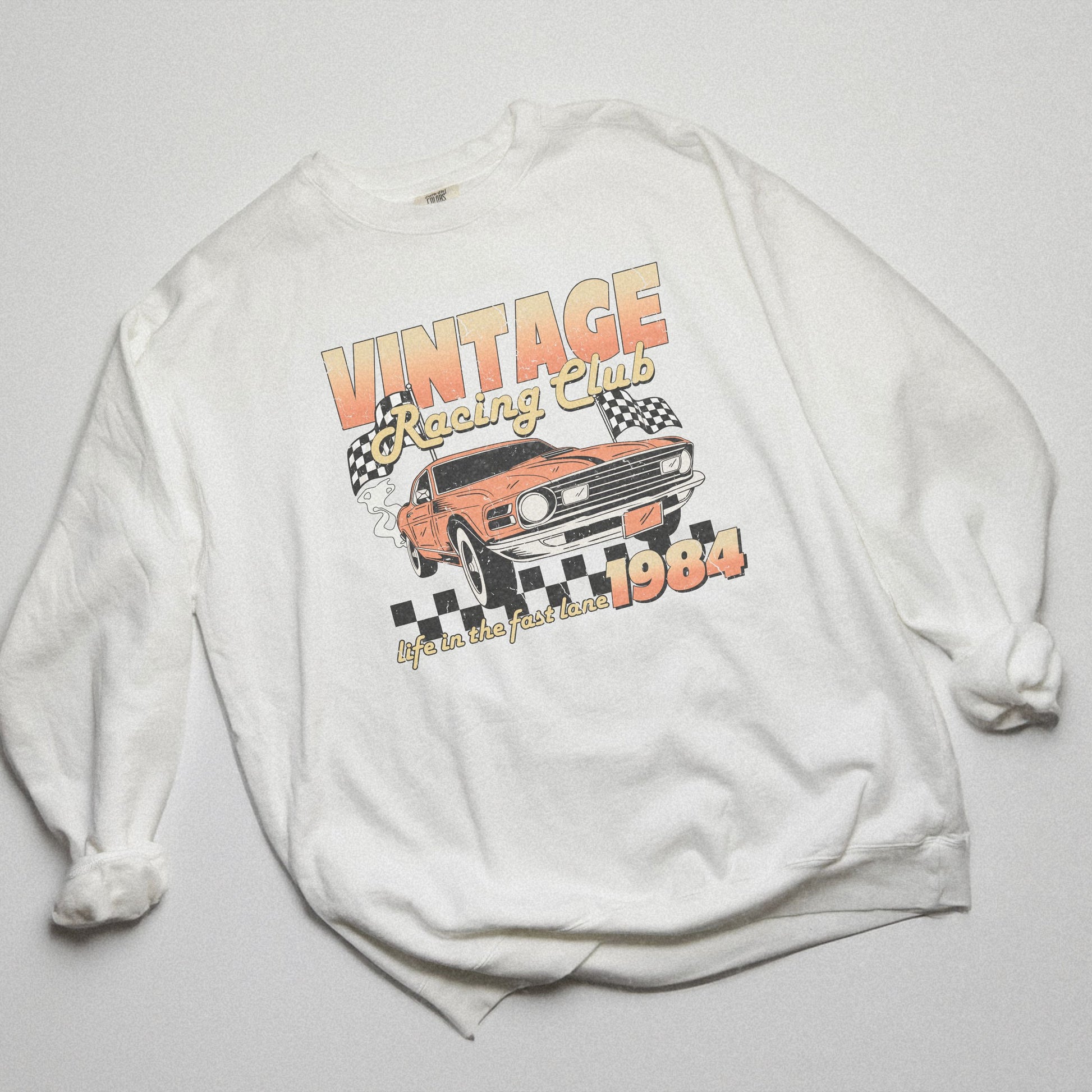 Retro car club shirt with vintage 1984 race car graphic, distressed design, and checkered flag accents. Perfect for muscle car lovers and fans of classic racing. Available as a crewneck sweatshirt in multiple colors.