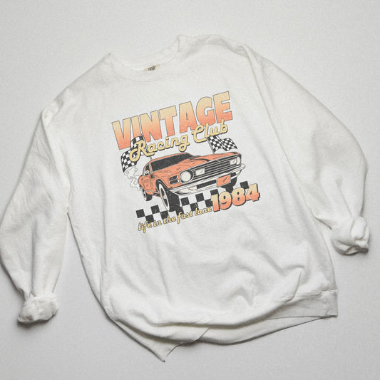 Retro car club shirt with vintage 1984 race car graphic, distressed design, and checkered flag accents. Perfect for muscle car lovers and fans of classic racing. Available as a crewneck sweatshirt in multiple colors.