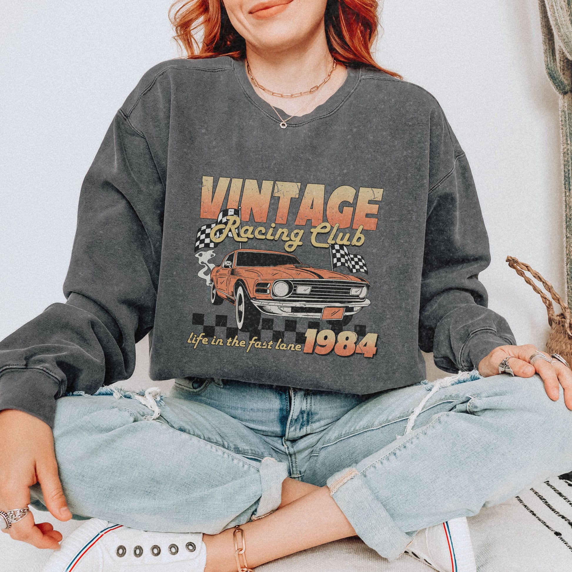 Retro car club shirt with vintage 1984 race car graphic, distressed design, and checkered flag accents. Perfect for muscle car lovers and fans of classic racing. Available as a crewneck sweatshirt in multiple colors.