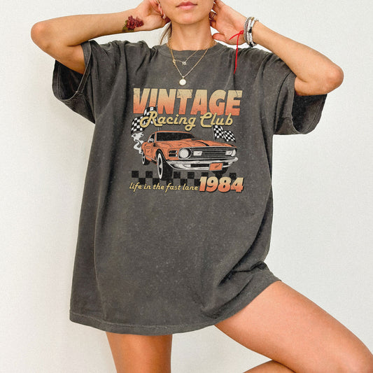 Retro racing T-shirt featuring a bold 1984 vintage design with distressed car graphics. Perfect nostalgic car shirt for muscle car lovers, featuring checkered flag details. Ideal for fans of old school racing and fast lane graphic tees.
